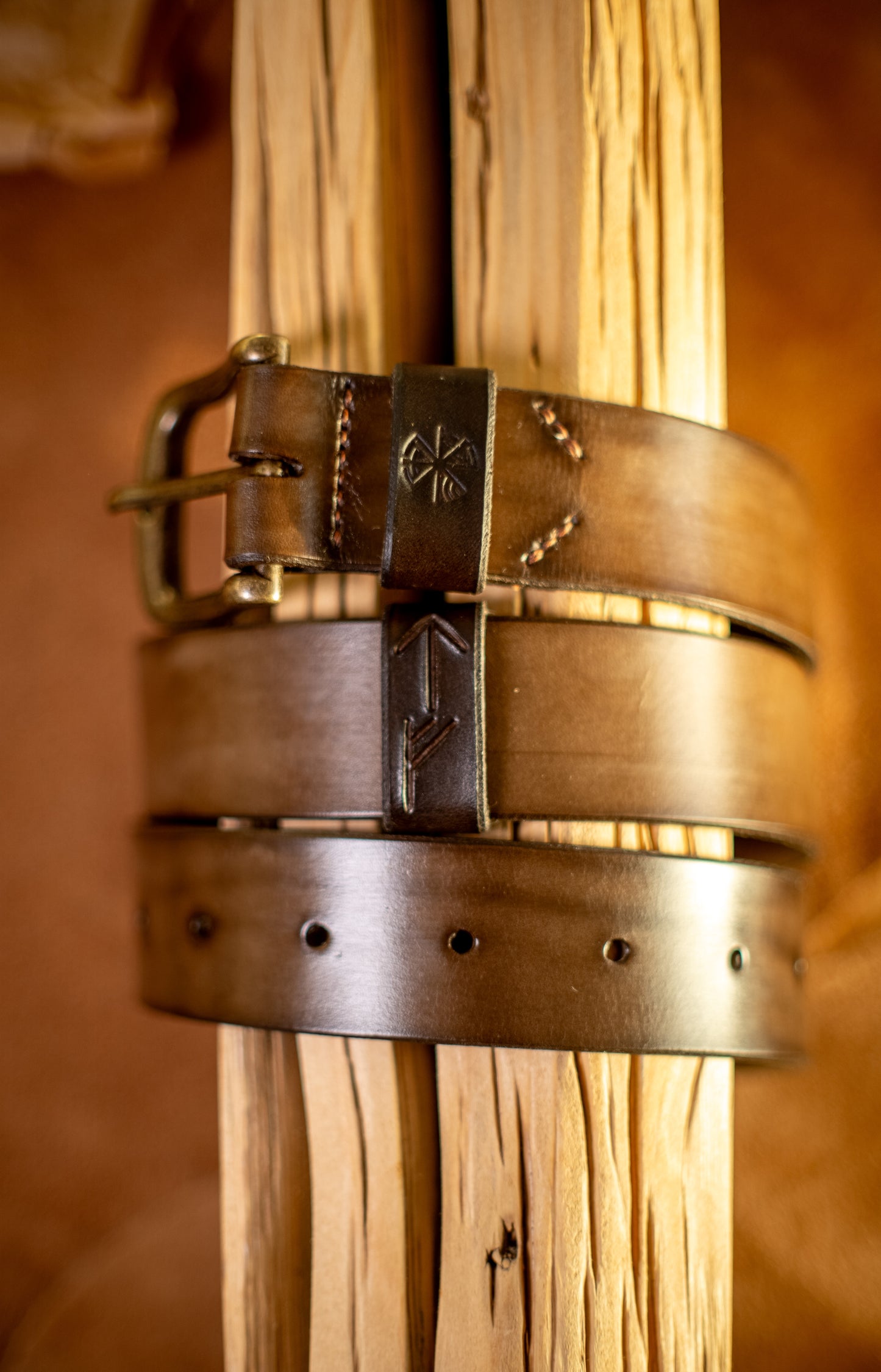 Et håndlaget lærbelte, Gleipnir 40mm, i en eksklusiv mørk sjokoladefarge, viklet rundt rustikt treverk. Beltet har en solid messingspenne, håndsydde detaljer og pregede symboler inspirert av norrøn mytologi. Den dype, mørke nyansen og den glatte overflaten fremhever den høye kvaliteten på læret, et tidløst og slitesterkt tilbehør designet for å vare i generasjoner.